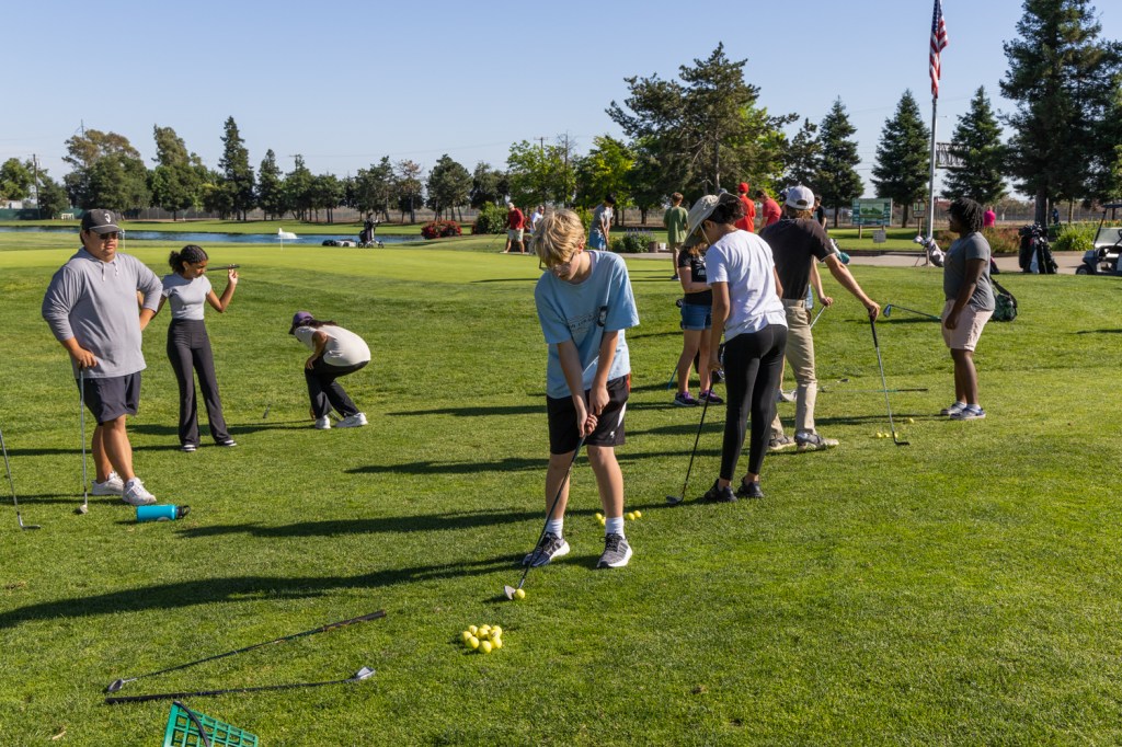 Young man in blue shirt readies his club during a class out on the golf course on a sunny day.